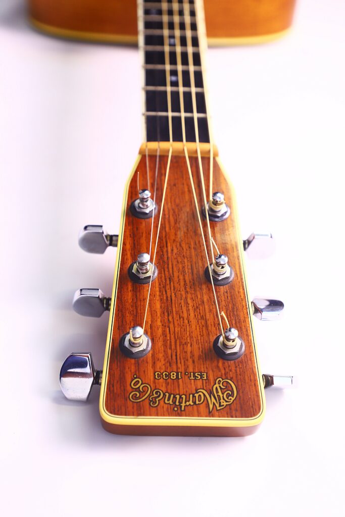 Close-Up Of The Headstock Of A Martin M-38 1979 Acoustic Guitar, Featuring Six Tuning Pegs, Metal Strings, And The Engraved Logo On Wood, All Set Against A White Background.
