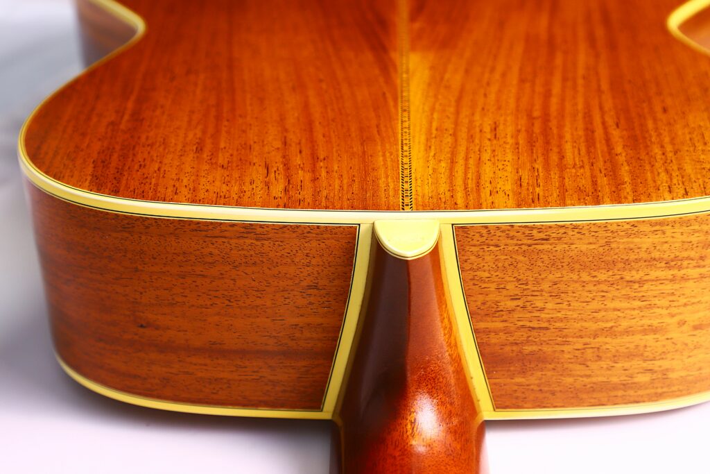 Close-Up Of The Back And Sides Of A Martin M-38 1979 Acoustic Guitar, Highlighting Polished Wood Grain, Yellow Binding, And The Neck Joint In Sharp Detail Against A White Background.