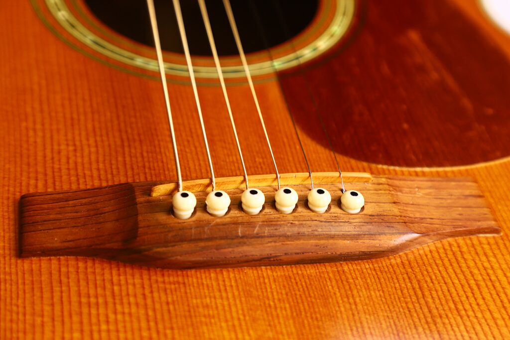 Close-Up Of The Martin M-38 1979 Acoustic Guitar’s Wooden Bridge With Six Strings And White Bridge Pins, Highlighting The Detailed Wood Grain And Part Of The Guitar Body.