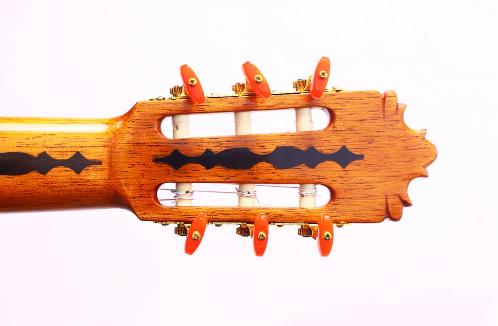 Close-Up Of The José Ruiz Pedregosa 2020 Classical Guitar Headstock, Featuring Wooden Tuning Pegs With Red Ends, Black Decorative Inlays, And Intricate Carved Details Against A White Background.