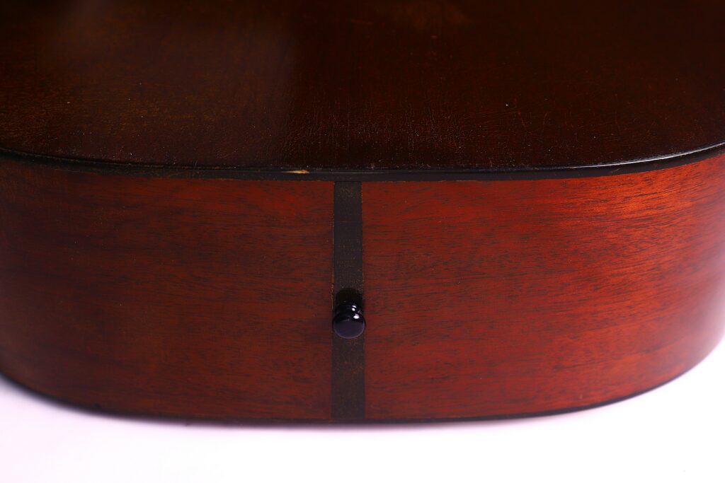 Close-Up Of The Bottom Edge Of A Martin D-18 1967 Acoustic Guitar, Featuring Dark Brown Polished Wood, A Black Strap Button At The Center, And A Vertical Seam In The Wood.