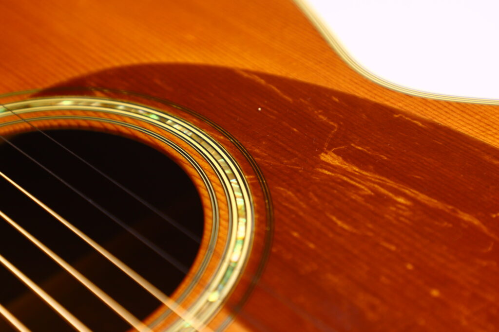 Close-Up Of A Martin M-38 1979 Acoustic Guitar Body, Featuring Wood Grain, Decorative Sound Hole Inlay, Metal Strings, And Visible Surface Scratches Highlighted By The Light.