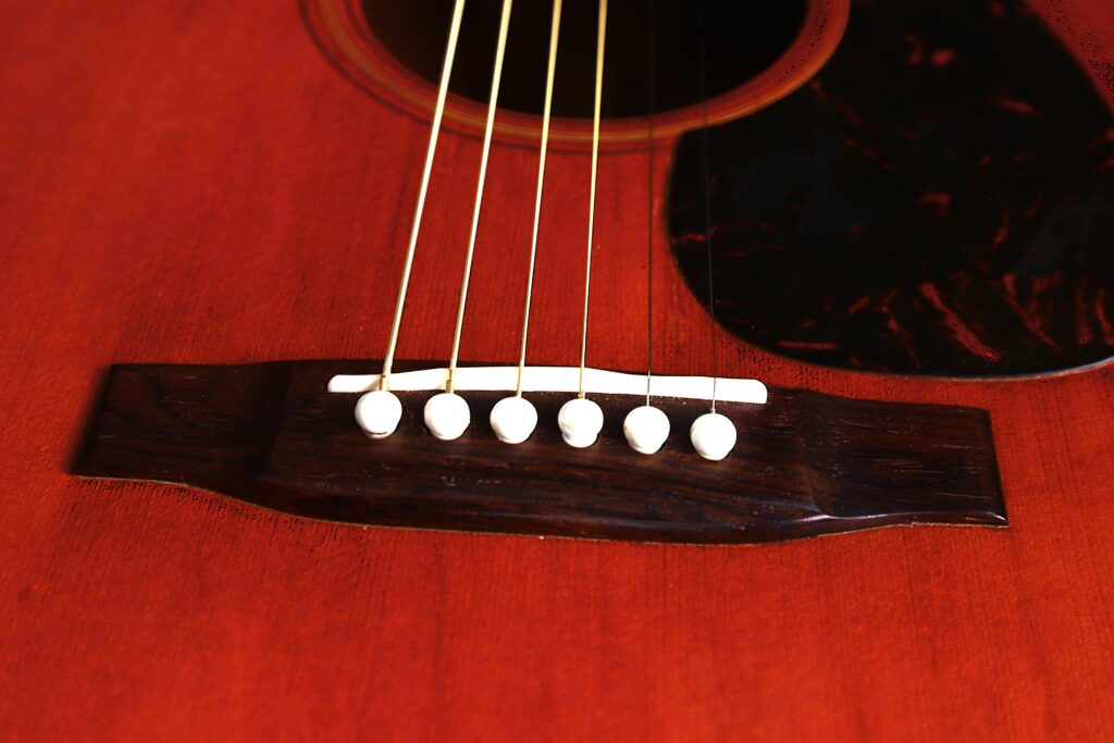 Close-Up Of The Bridge And Six White Pins Securing The Strings On A Polished Wooden Body Of A Martin D-18 1967 Acoustic Guitar.