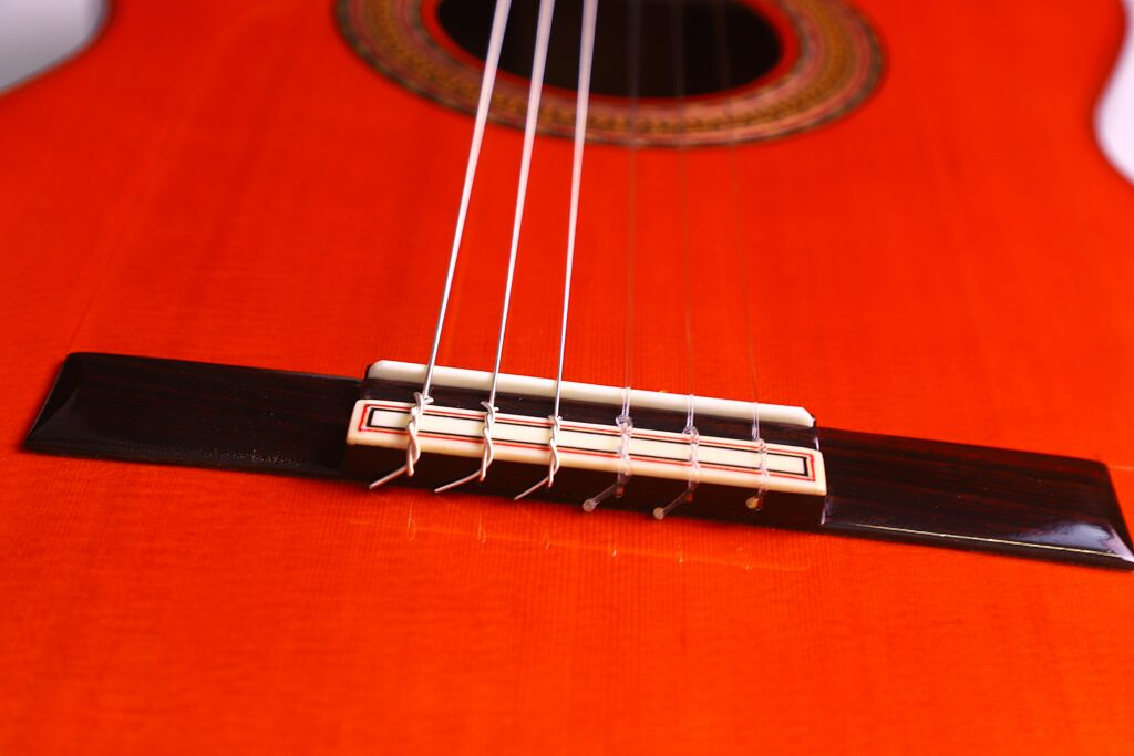 Close-Up Of The Hermanos Conde 1999 Paco De Lucia Special Flamenco Guitar, Highlighting Its Bright Orange Finish, Dark Wooden Bridge, And Strings Running Toward The Sound Hole.