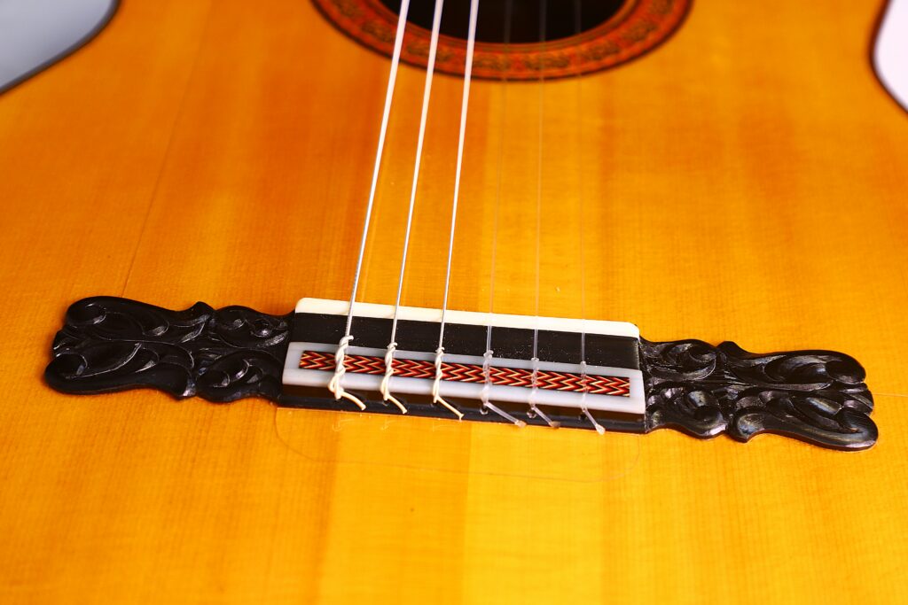 Close-Up Of The José Ruiz Pedregosa 2020 Classical Guitar Bridge, Featuring Intricate Black Carvings, Six Strings, And Decorative Wooden Body Patterns.