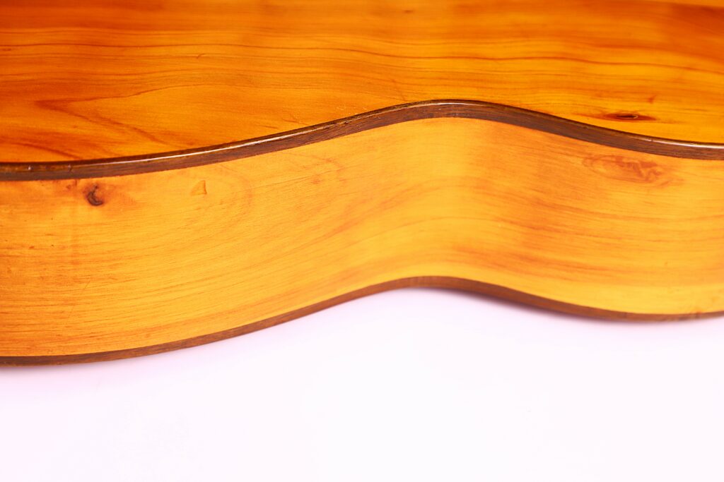 Close-Up Of The Augustin Gaspar Cebrian 1935 Classical Guitar’s Side, Highlighting Its Smooth, Polished Wooden Body And Natural Wood Grain Against A White Background.