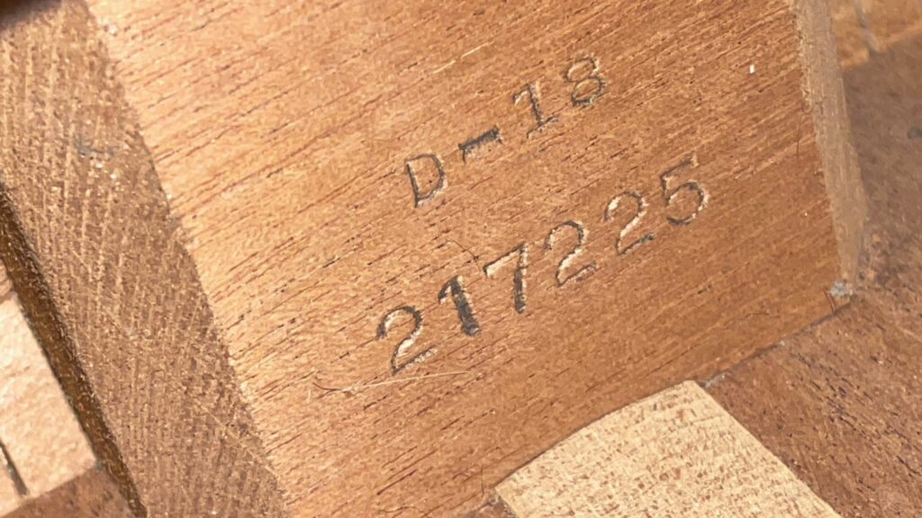 Close-Up Of A Martin D-18 1967 Acoustic Guitars Wooden Surface, Showing The Engraved Text “D-18” And Serial Number “217225.” The Wood Grain And Texture Are Clearly Visible.
