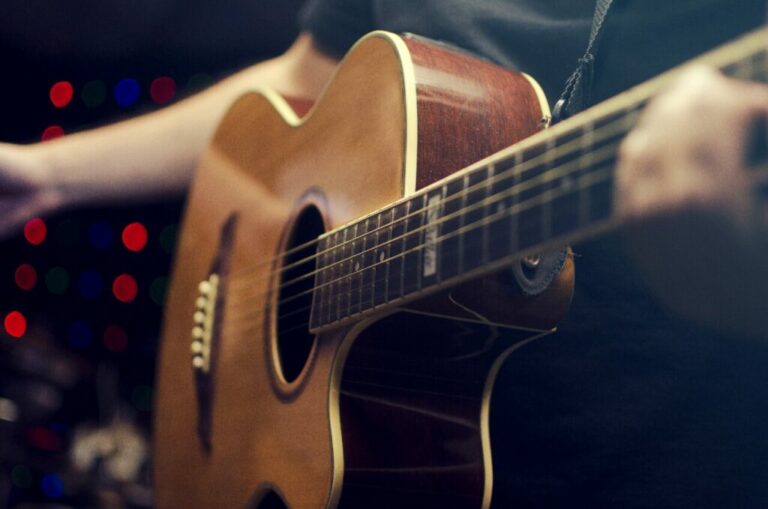 Berühmte Gitarristen - Nahaufnahme einer Person, die eine akustische Gitarre spielt, mit der rechten Hand auf den Saiten