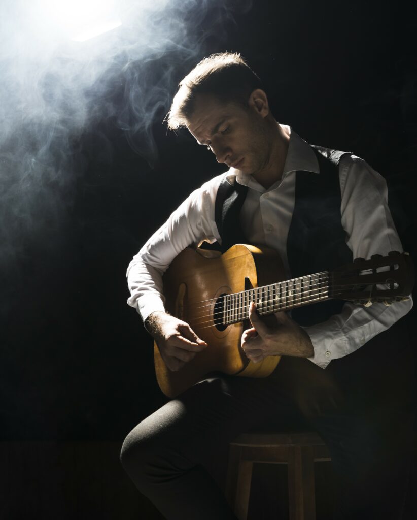 Die Top 10 der klassischen Gitarristen aller Zeiten - Ein Mann in weißem Hemd und dunkler Weste sitzt auf einem Hocker und spielt auf einer klassischen Gitarre