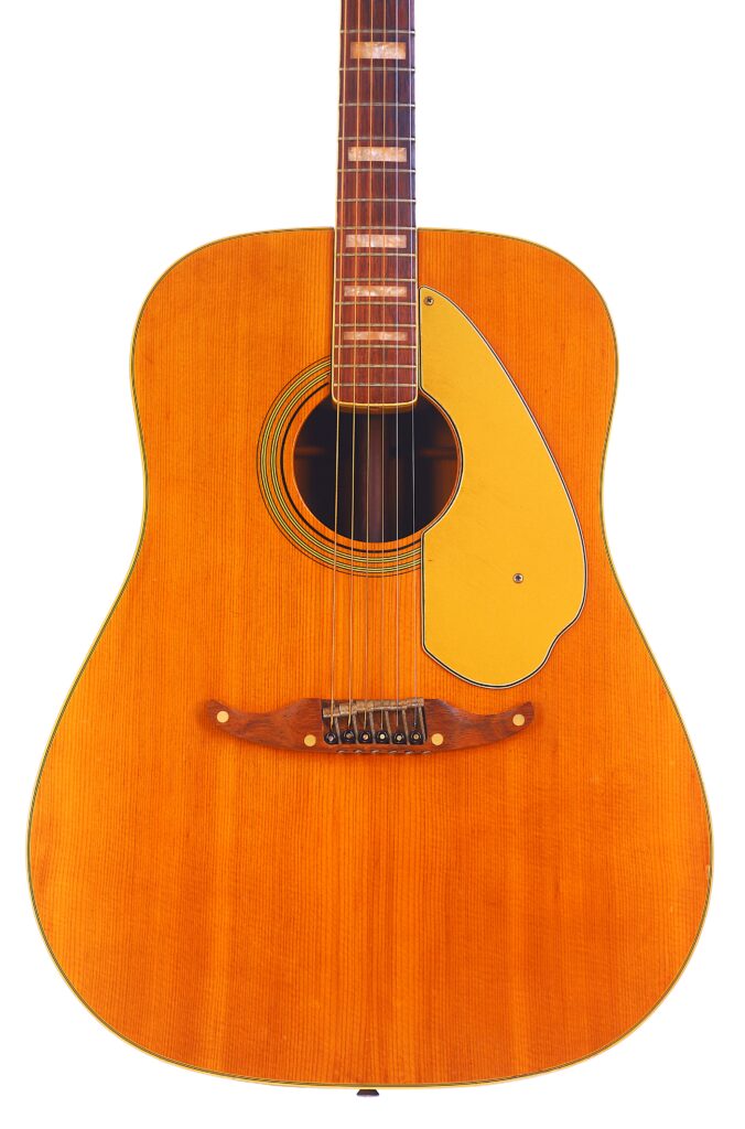 A Close-Up Of The Fender Wildwood 1967 Acoustic Guitar Displays Its Natural Wood Finish, Highlighting The Body, Pickguard, Bridge, Strings, And Lower Part Of The Neck.