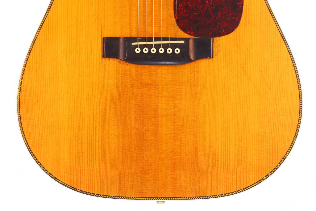 Close-Up Of The Lower Half Of A Martin Hd-35 1979 Acoustic Guitar, Showing Its Light Wood Finish, Dark Bridge With Six Pins, And Tortoiseshell-Colored Pickguard.