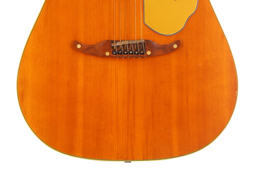 Close-Up Of The Lower Body Of A Fender Wildwood 1967 Acoustic Guitar, Highlighting The Wooden Bridge, Strings, And Pickguard On A Warm Orange-Brown Wood Finish.