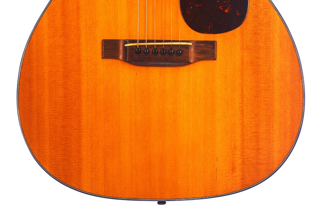 Close-Up Of The Lower Half Of A Martin 000-18 1950 Acoustic Guitar, Highlighting Its Wooden Body, Bridge, Strings, And A Portion Of The Pickguard Set Against A White Background.