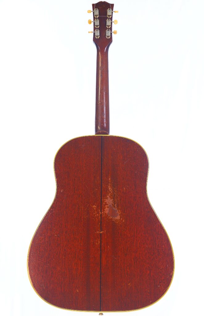 Back View Of The Gibson Southern Jumbo 1955 Acoustic Guitar, Highlighting Its Wooden Finish, Visible Neck, Tuning Pegs, And Noticeable Wear Marks On The Body.