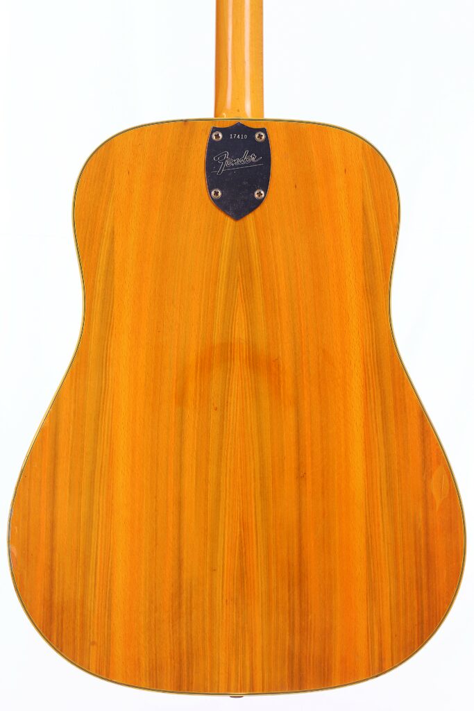 The Image Shows The Back Of A Fender Wildwood 1967 Acoustic Guitar, Featuring A Smooth, Light Wood Finish With Subtle Vertical Grain Patterns And A Black Plate Near The Neck Displaying Text And A Serial Number.