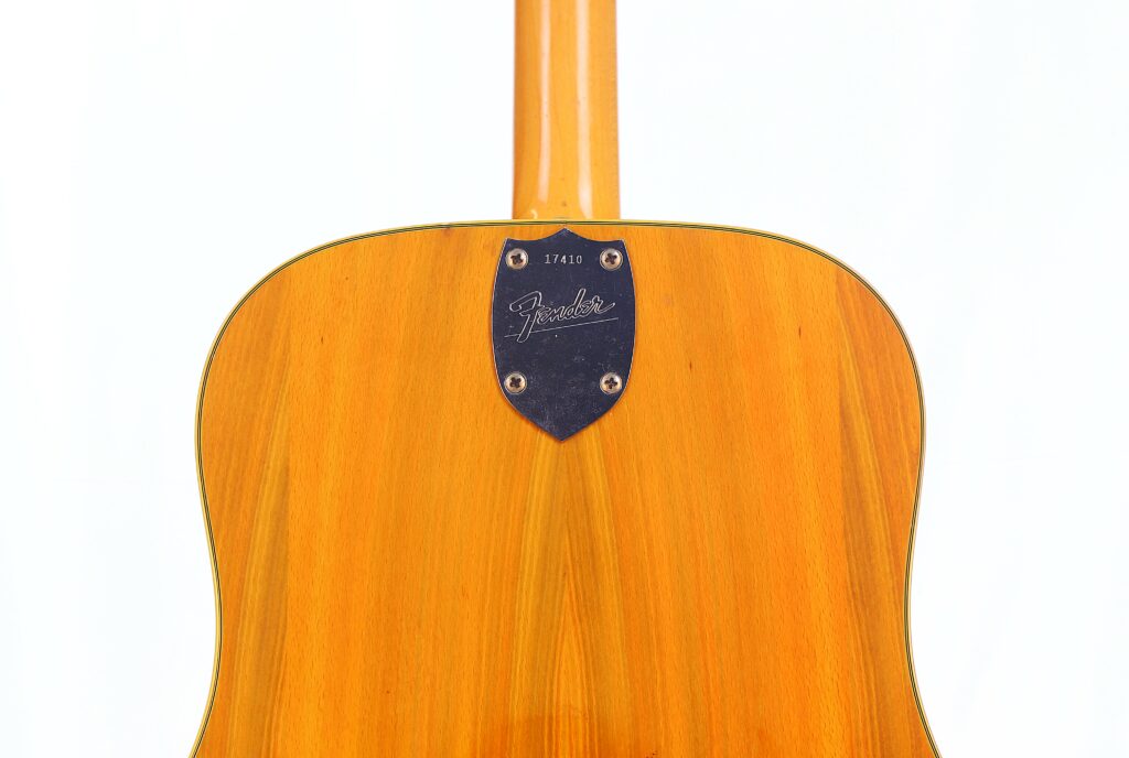 Close-Up Of The Back Of A Fender Wildwood 1967 Acoustic Guitar, Showcasing Its Natural Wood Finish And Metal Neck Plate Engraved With Fender And The Number 17410, Set Against A White Background.