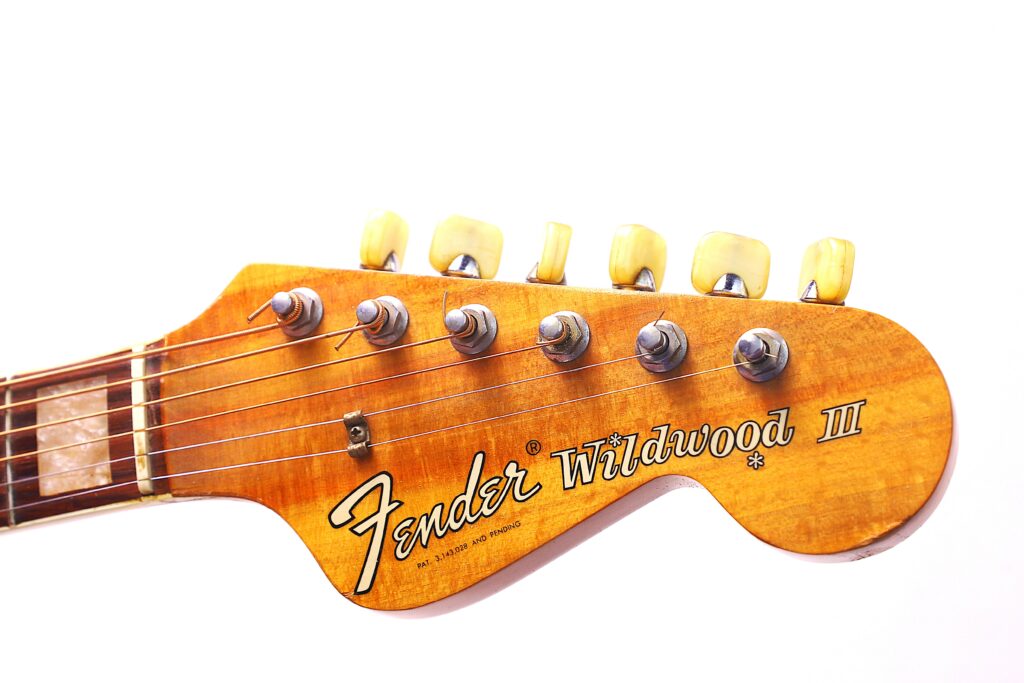 Close-Up Of The Fender Wildwood 1967 Acoustic Guitar Headstock, Displaying Tuning Pegs, Strings, And The Logo On A Wood Grain Finish Against A White Background.