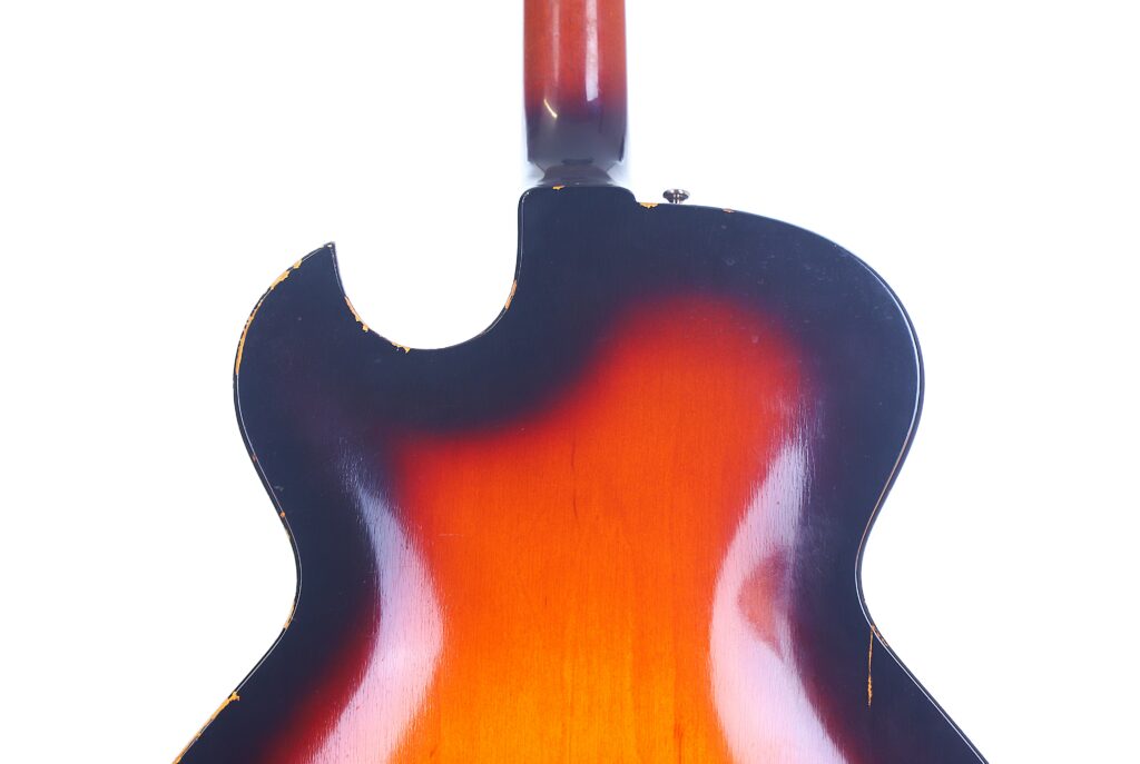 The Image Displays The Back Of A Guild T-100D Slim Jim 1967 Electric Guitar, Featuring Its Sunburst Finish, Glossy Surface, And Wood Grain Detail Against A White Background.