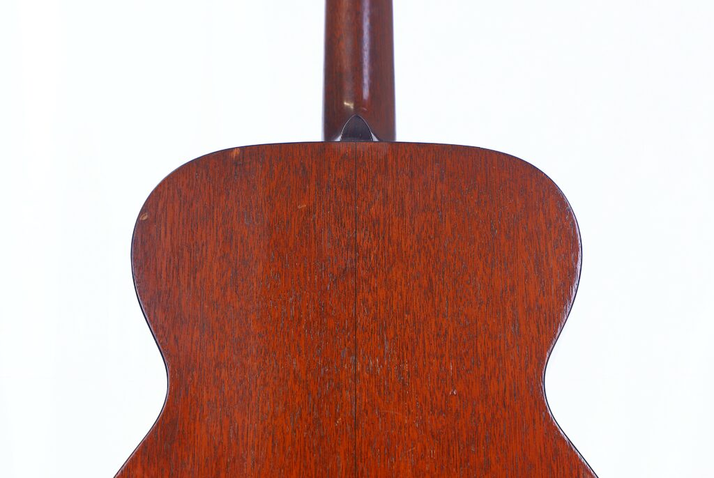 The Image Shows The Back Of A Martin 000-18 1950 Acoustic Guitar With A Reddish-Brown Wooden Finish, Highlighting Its Wood Grain And Texture. The Guitar’s Neck Is Partially Visible At The Top Against A White Background.