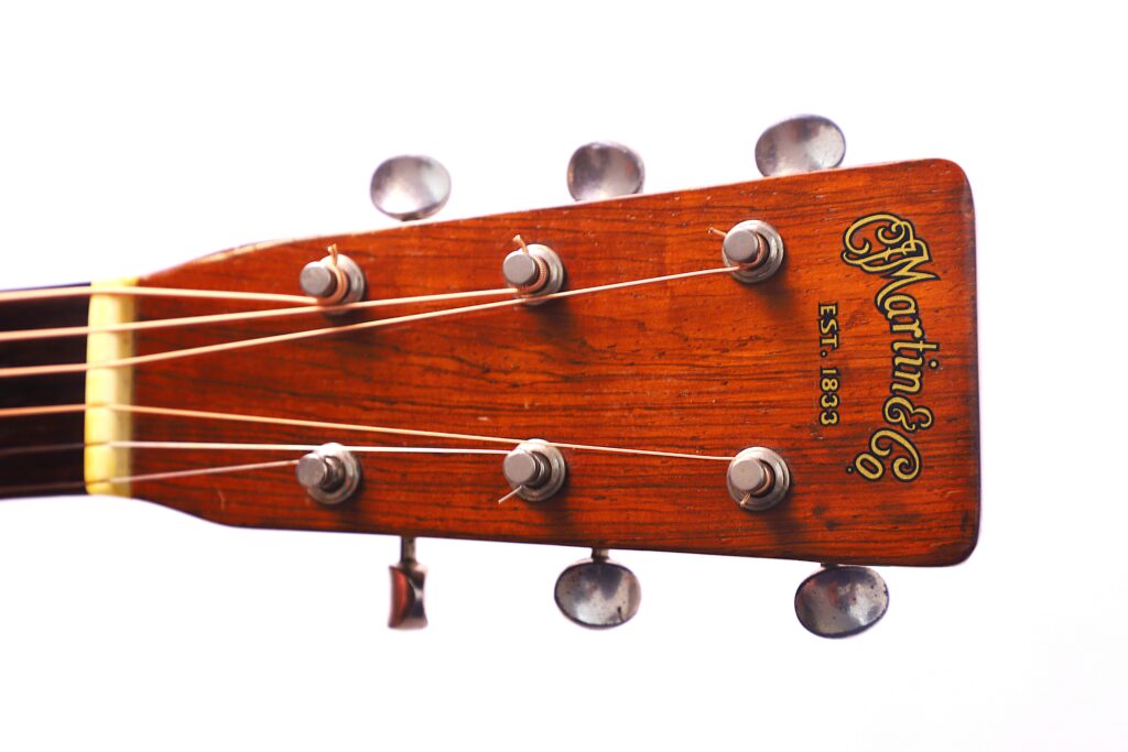 Close-Up Of A Martin 000-18 1950 Acoustic Guitar Headstock With Six Tuning Pegs, Guitar Strings, Company Logo, And Est. 1833 Text On Polished Wood, Set Against A White Background.