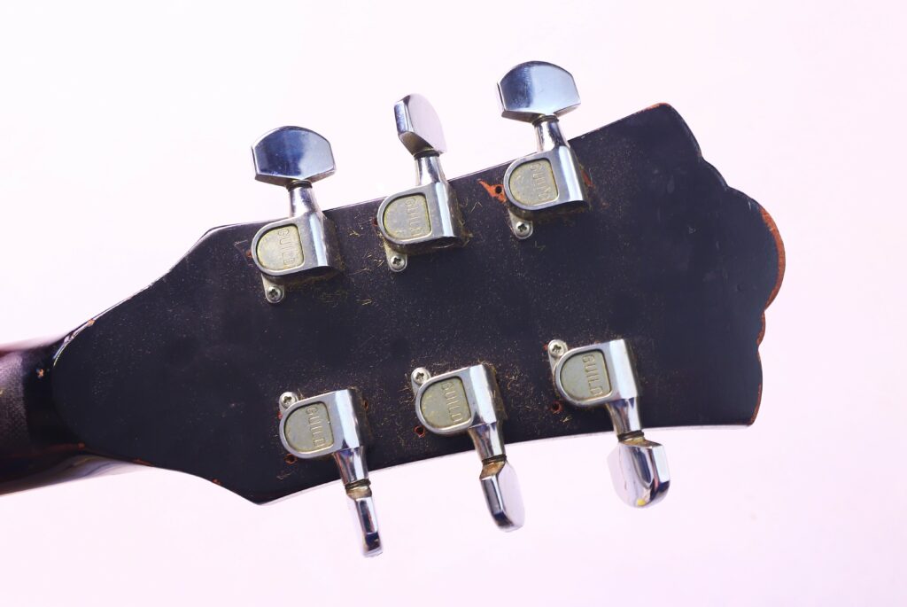 Close-Up Of The Guild T-100D Slim Jim 1967 Electric Guitar Headstock Back, Highlighting Its Six Silver Tuning Pegs Against A Light Background.