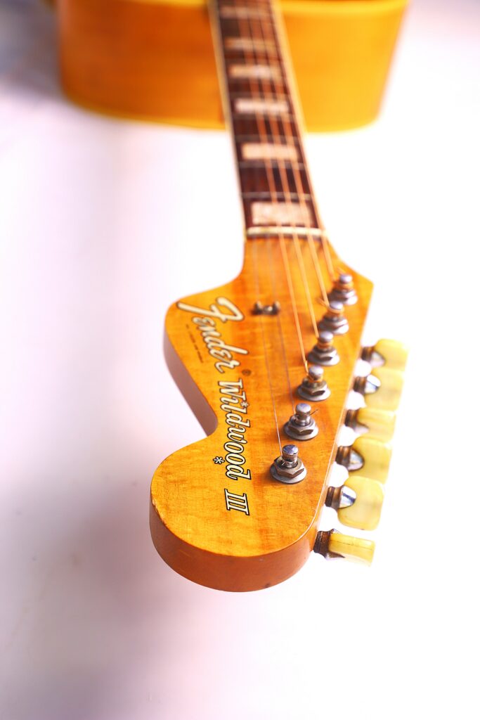 Close-Up Of The Headstock Of A Fender Wildwood 1967 Acoustic Guitar, Highlighting The Tuning Pegs And Logo, With A Partial View Of The Neck And Body In The Background.