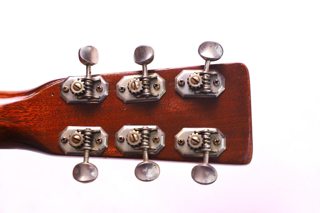 Close-Up Of The Back Of A Martin 000-18 1950 Acoustic Guitar Headstock, Displaying Six Metal Tuning Pegs And Machine Heads Against A White Background.