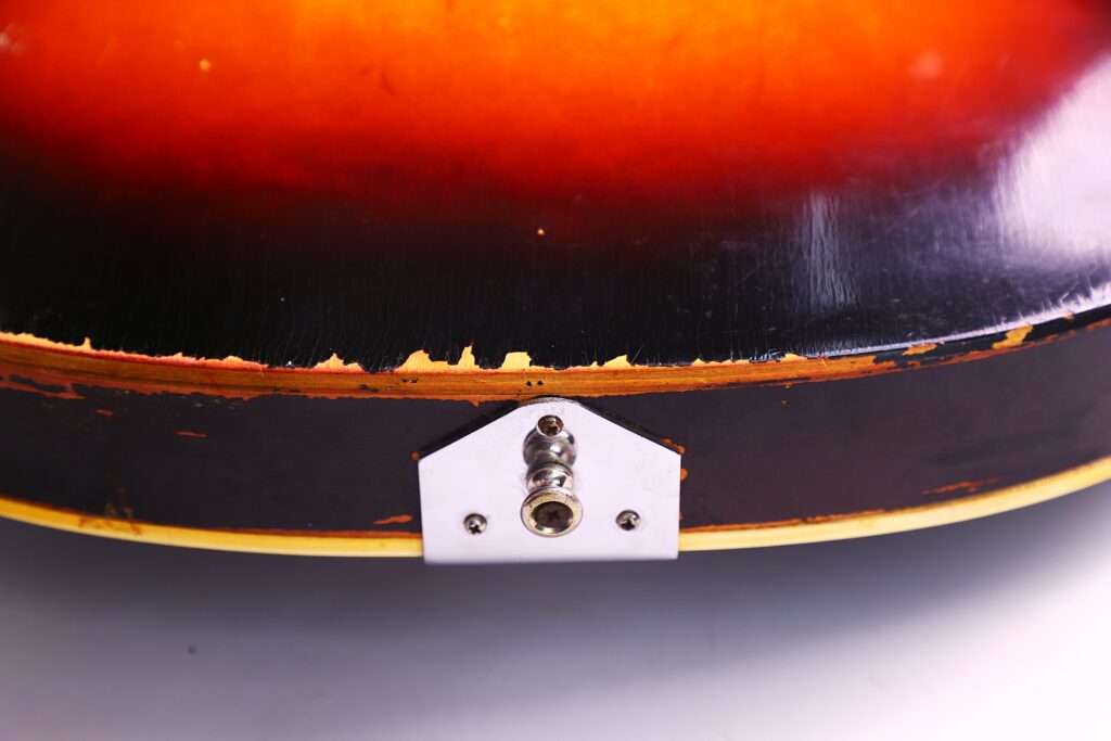 Close-Up Of The Worn Edge On A Guild T-100D Slim Jim 1967 Electric Guitar, Highlighting Chipped Sunburst Paint And The Metal Input Jack Plate At The Bottom Center.