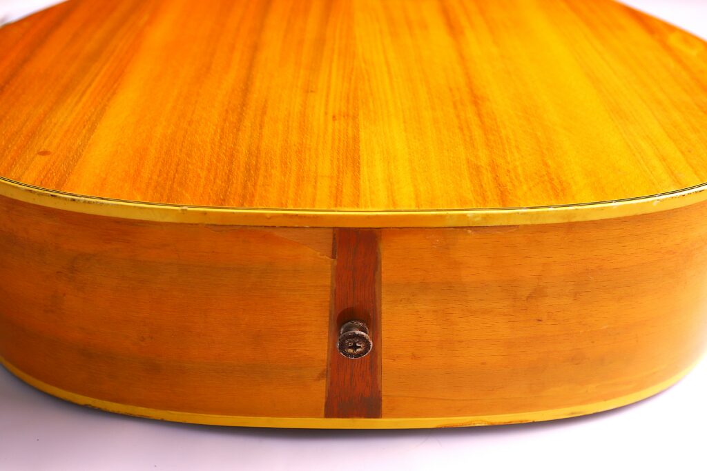 Close-Up View Of The Back And Bottom Edge Of A Fender Wildwood 1967 Acoustic Guitar, Highlighting Its Light Brown Wooden Finish And Centrally Positioned Metal Input Jack.