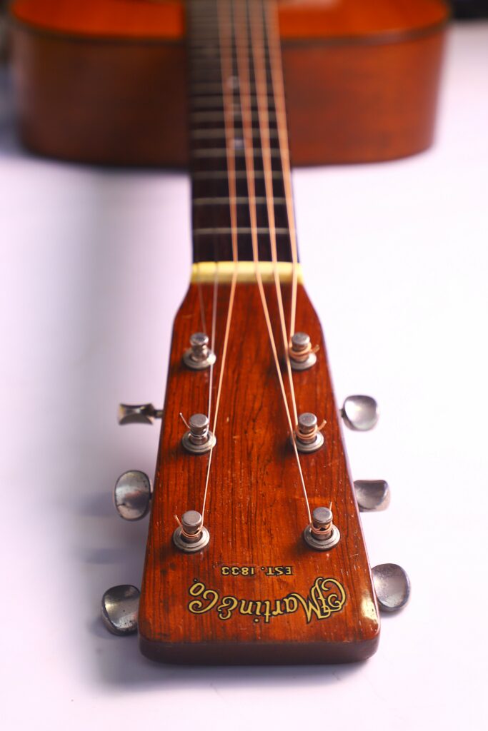 Close-Up View Of The Martin 000-18 1950 Acoustic Guitars Brown Headstock And Tuning Pegs, With The Martin &Amp; Co. Logo Visible. The Guitar Neck Extends Toward The Body, Resting On A White Surface.