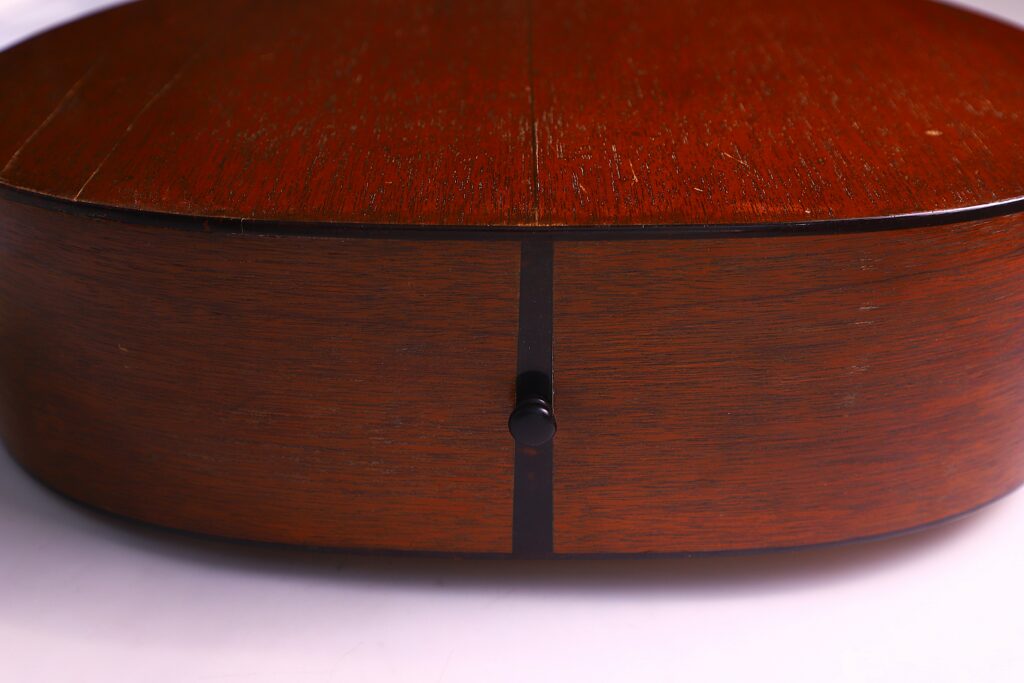 Close-Up Of The Martin 000-18 1950 Acoustic Guitar’s Side, Highlighting The Wood Grain, A Centered Black Strap Button, And A Vertical Dark Line. Background Is White.