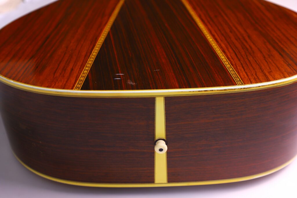 Close-Up Of The Back Of A Martin Hd-35 1979 Acoustic Guitar With A Glossy Dark Wood Finish, Two Decorative Yellow Stripes, Yellow Edge Trim, And A Small White Strap Button At The Base.