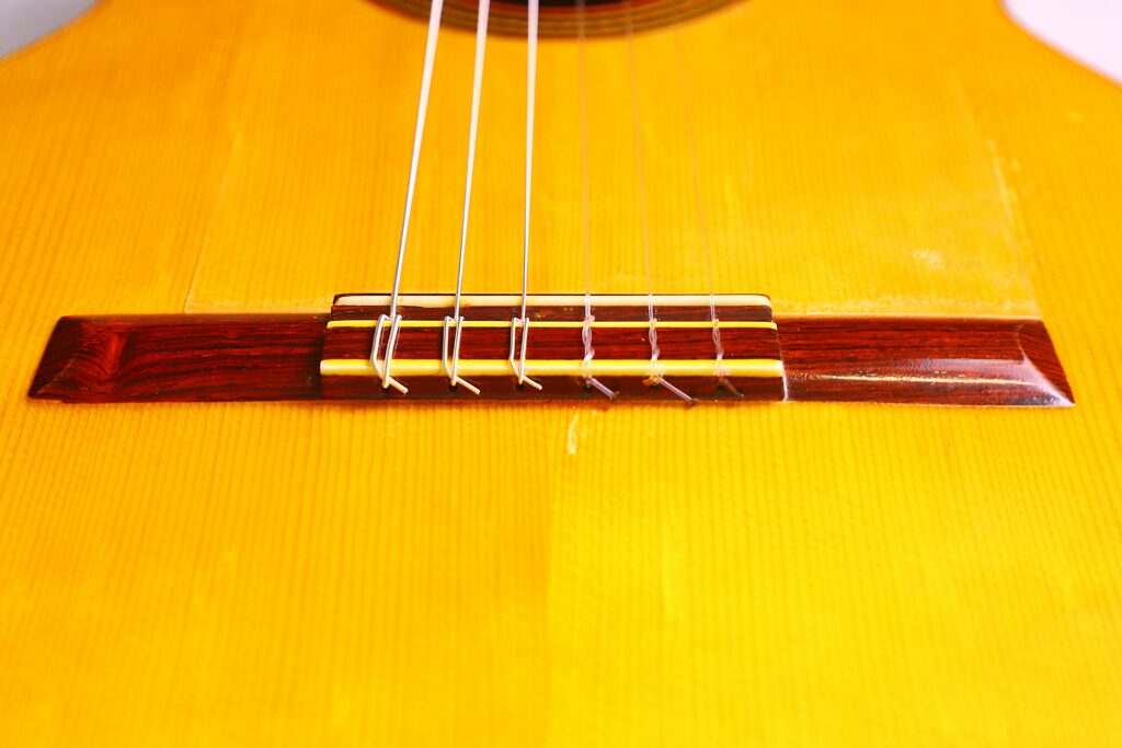 Close-Up Of The Bridge And Strings On A Conde Hermanos 1971 Flamenco Guitar, Highlighting The Wood Grain And Detailed String Attachments On Its Bright Yellow Body.