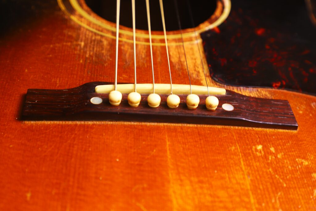 Close-Up Of The Bridge And Strings On The Gibson Southern Jumbo 1955 Acoustic Guitar, Showcasing Its Detailed Wood Grain And Worn Vintage Finish.