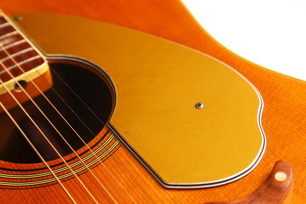 Close-Up Of A Fender Wildwood 1967 Acoustic Guitar, Featuring The Sound Hole, Strings, And Golden Pickguard On A Wooden Body With Detailed Grain And Inlay.