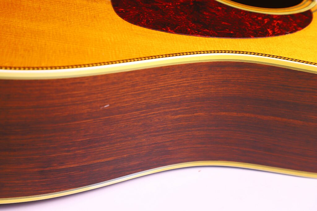 Close-Up Of The Side Of A Martin Hd-35 1979 Acoustic Guitar, Highlighting The Wood Grain, Yellow Trim, And Part Of The Pickguard On The Top Surface.