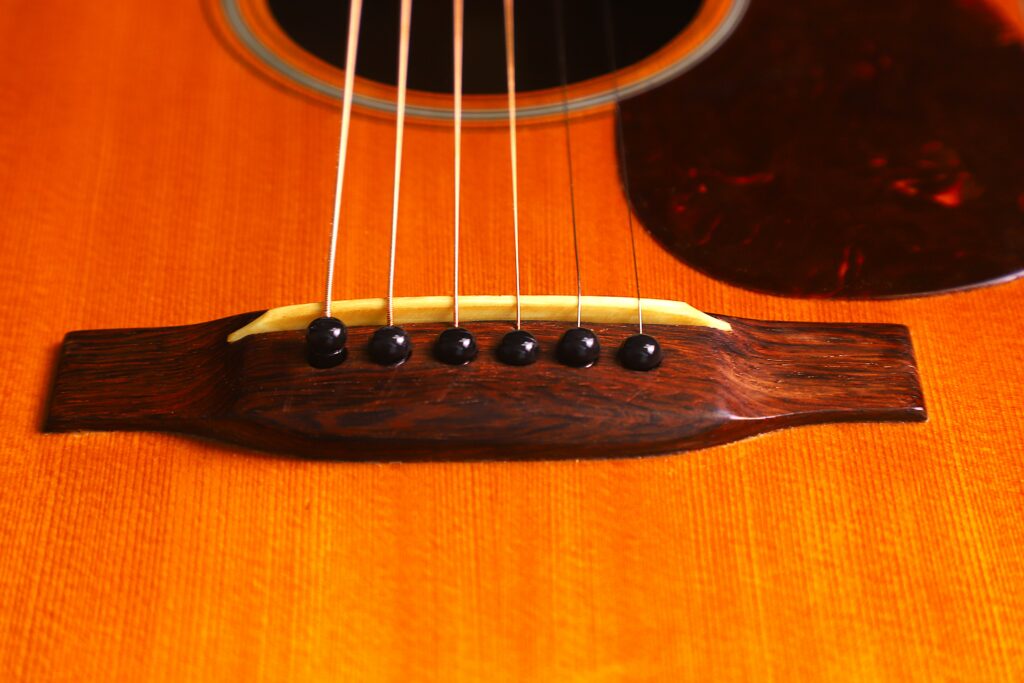 Close-Up Of The Martin 000-18 1950 Acoustic Guitars Bridge And Strings, Highlighting Its Wooden Body, Dark Bridge Pins, And Detailed Wood Grain Under Warm Lighting.