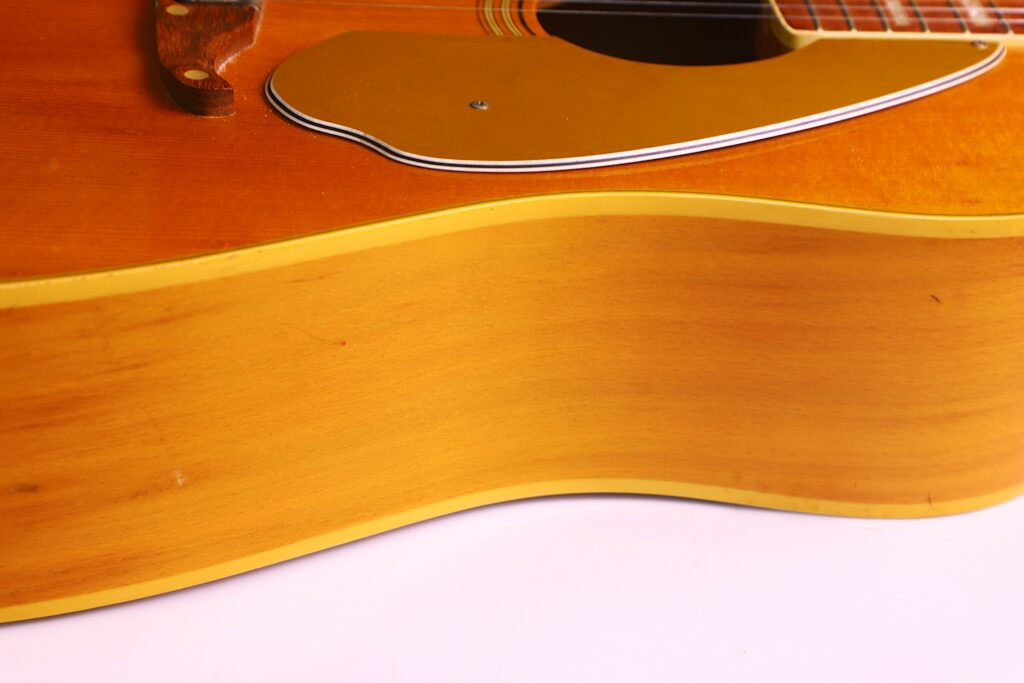 Close-Up View Of The Side And Body Of A Fender Wildwood 1967 Acoustic Guitar With A Light Wood Finish, Showing Part Of The Pickguard And Strings Against A White Background.