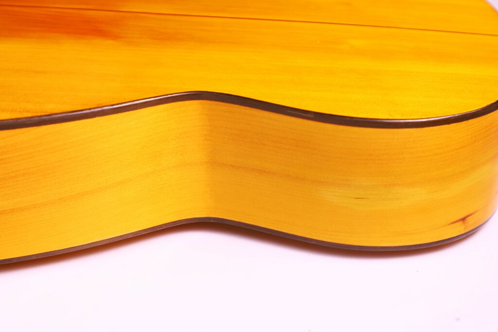 Close-Up Of The Side And Back Of A Conde Hermanos 1971 Flamenco Guitar, Highlighting Its Smooth, Glossy Yellow Finish And Dark Edges Against A White Background.