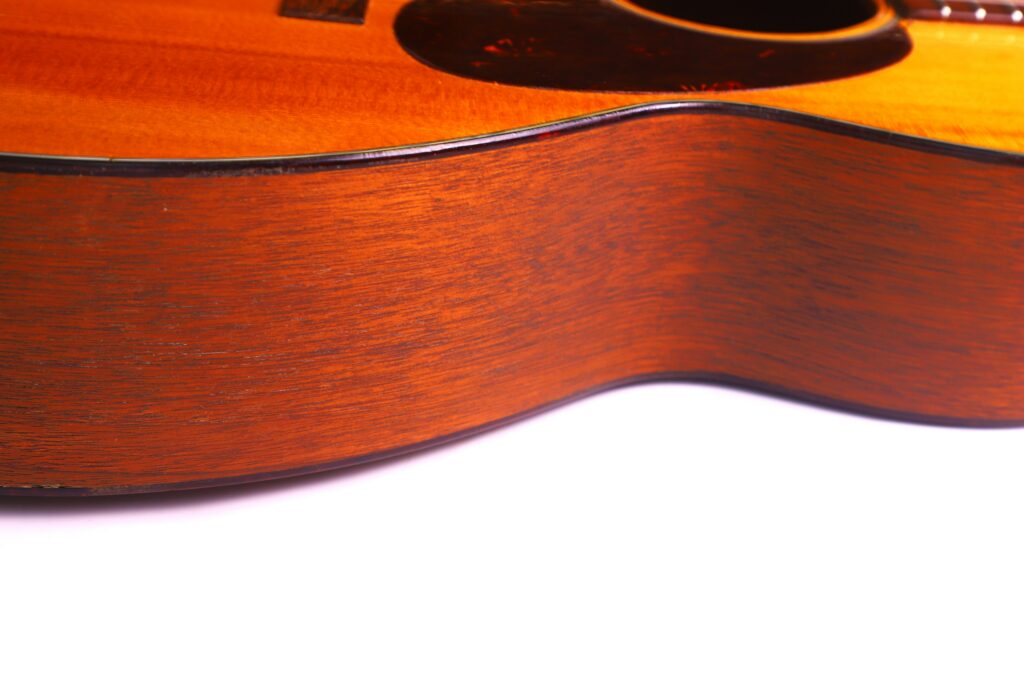 Close-Up Of The Side Of A Martin 000-18 1950 Acoustic Guitar, Featuring Detailed Wood Grain And Warm Brown Finish, With Part Of The Guitar’s Body And Sound Hole Visible Against A White Background.