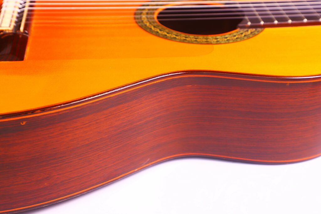 Close-Up Of A Hermanos Conde 1986 Paco De Lucia Flamenco Guitar Highlighting The Curved Wooden Side, Partial Strings, And Decorative Inlay Around The Sound Hole, All Set Against A White Background.