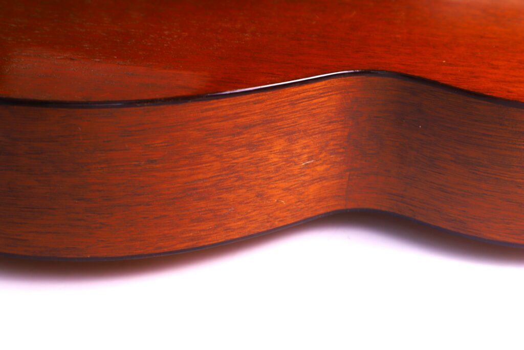 Close-Up Of The Side Of A Martin 000-18 1950 Acoustic Guitar, Highlighting Its Smooth, Polished Reddish-Brown Wood Grain And Gentle Curves Against A White Background.