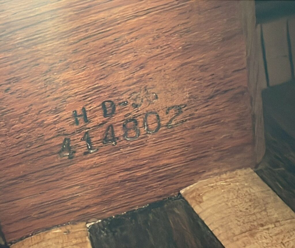 A Close-Up Of A Martin Hd-35 1979 Acoustic Guitar Shows Its Wooden Surface With “H D-36 414802” Stamped In Black Ink, Highlighting The Rough Texture And Color Variations.