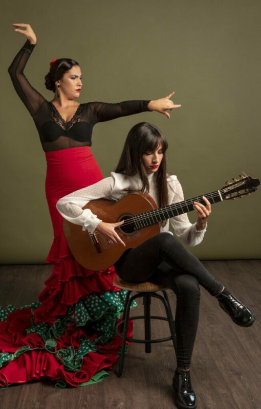 The Flamenco Guitar And Flamenco As A World Cultural Heritage - A Woman In A Red Flamenco Dress Poses With Raised Arms Behind Another Woman Seated On A Stool, Playing A Flamenco Guitar