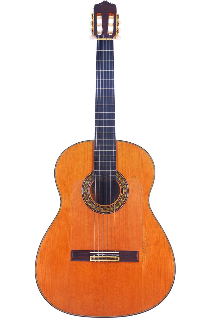 A Gerundino Fernandez 1990 Flamenco Guitar With A Wooden Body, Six Strings, Dark Fingerboard, And Decorative Soundhole Rosette Is Displayed Upright On A White Background.
