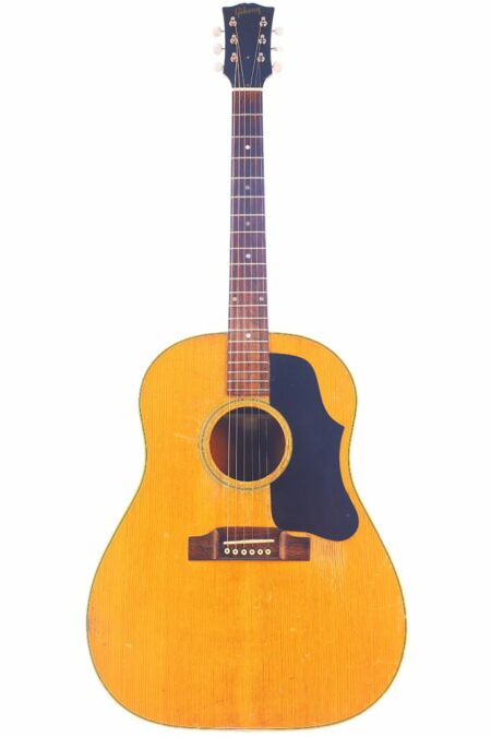 A Gibson J-50 1956 Acoustic Guitar featuring a natural finish, black pickguard, six strings, and visible wear is shown against a white background.