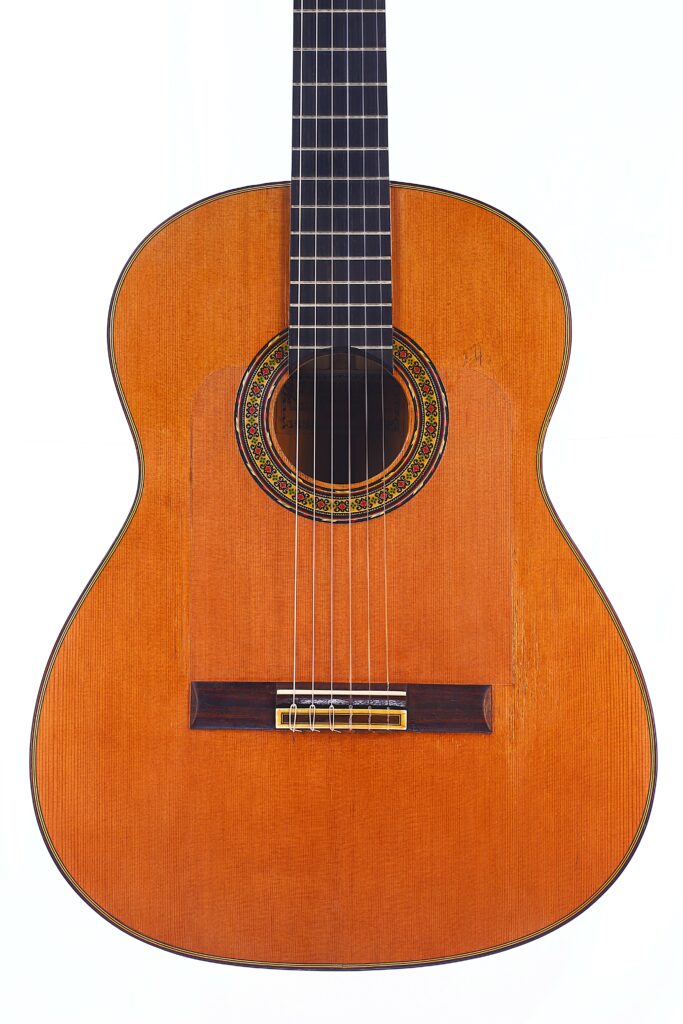 A Gerundino Fernandez 1990 Flamenco Guitar With A Wooden Body, Six Strings, And A Decorative Rosette Around The Sound Hole Is Shown Against A White Background.