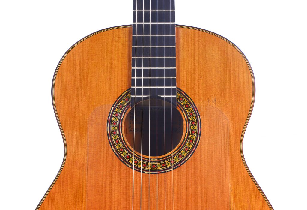 Close-Up Of The Gerundino Fernandez 1990 Flamenco Guitar, Highlighting Its Wooden Texture, Decorative Rosette Around The Sound Hole, And Nylon Strings Set Against A White Background.
