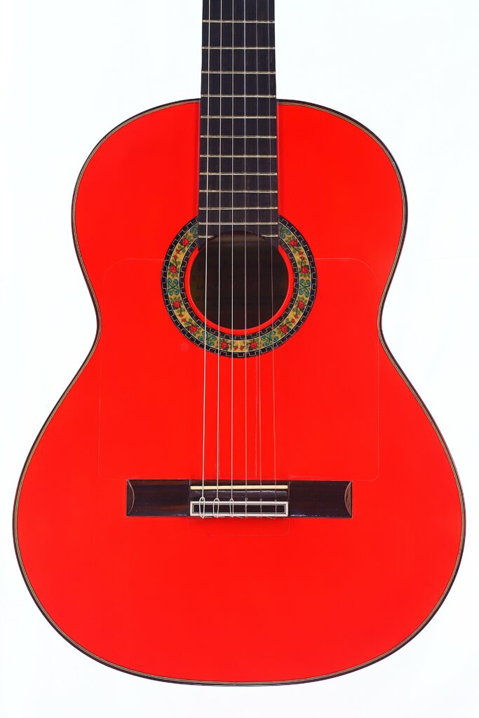A Pedro Fernández Luque 2021 Blanca Flamenco Guitar In Bright Red With Intricate Sound Hole Decorations, Shown Against A White Background.
