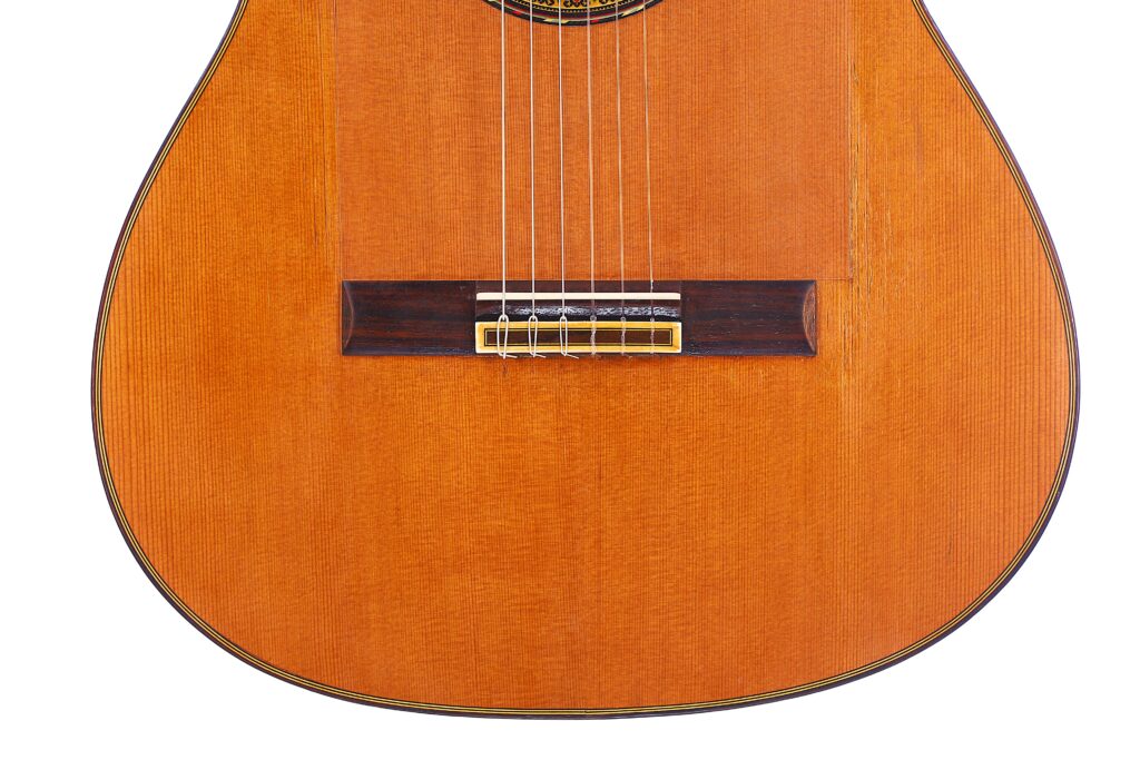 Close-Up Of The Gerundino Fernandez 1990 Flamenco Guitar’s Lower Half, Featuring Its Strings, Bridge, And A Natural-Finish Wooden Body.